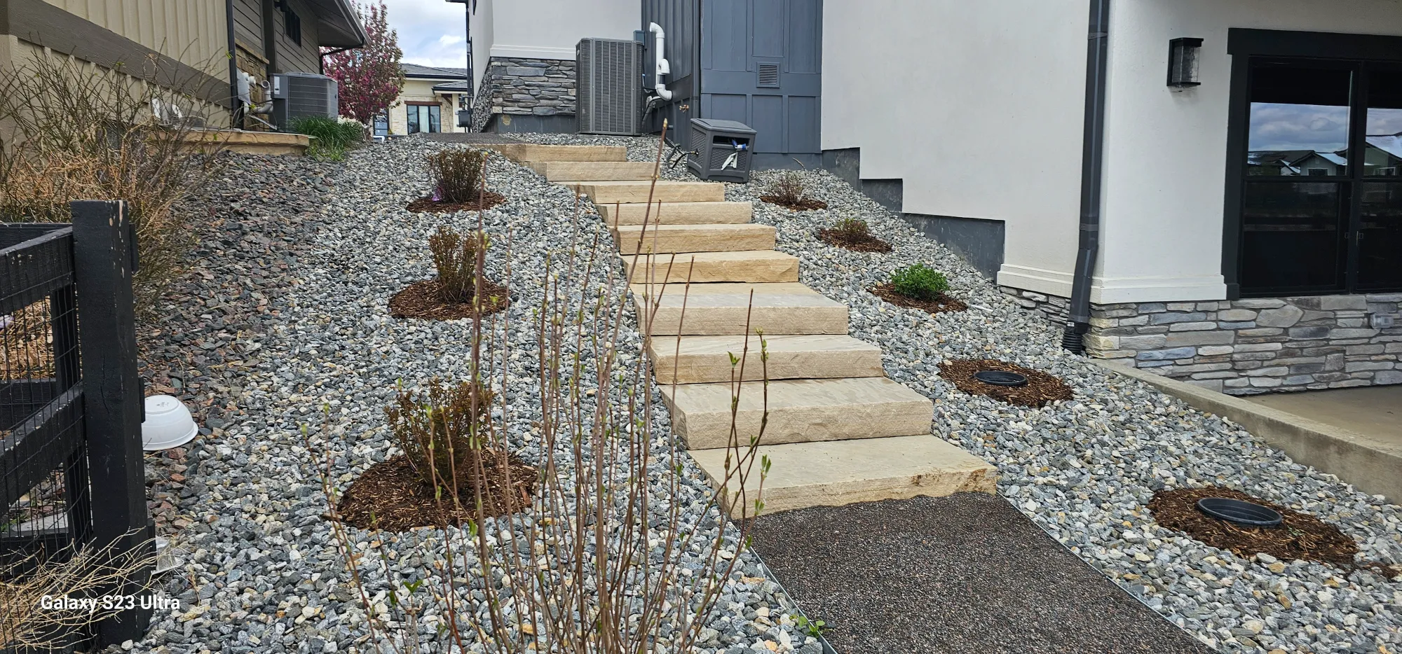 Sandstone slab steps installed on a gravel slope next to a modern home with stone veneer accents.