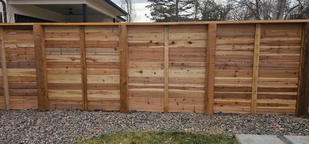 Close-up of a high-quality horizontal cedar privacy fence with sturdy wooden posts set over a decorative rock border.
