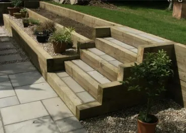 A multi-level wooden timber retaining wall featuring integrated steps and planter boxes on a stone patio.
